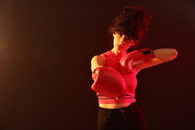 Photo of Beautiful young woman with boxing gloves on color background in neon lights. Space for text