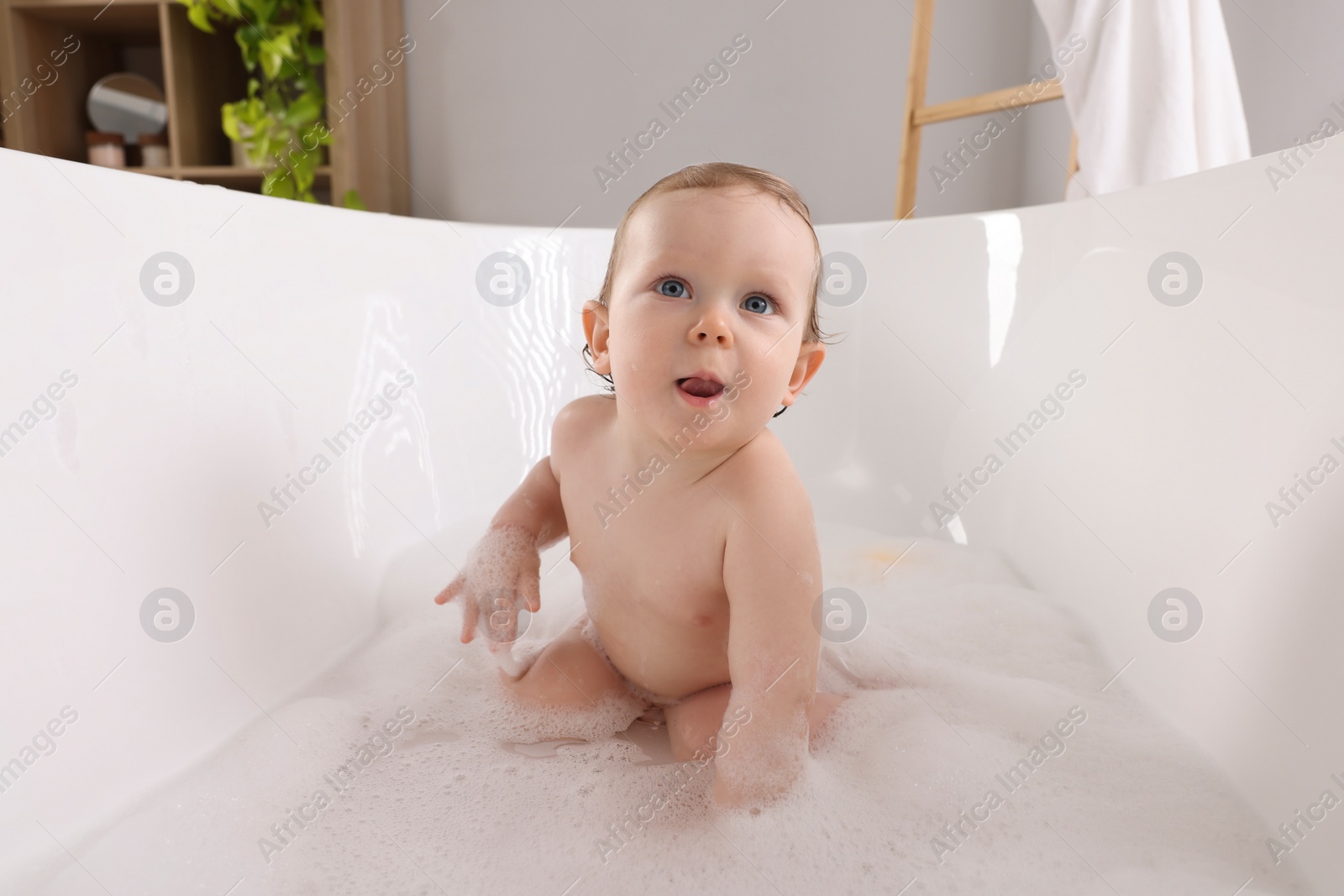 Photo of Cute little baby taking foamy bath at home