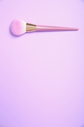 Photo of Professional makeup brush on lilac background, top view. Space for text