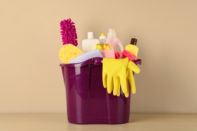 Photo of Bucket with different cleaning supplies on wooden floor near beige wall