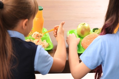 Photo of Little girls at table with healthy food in school canteen