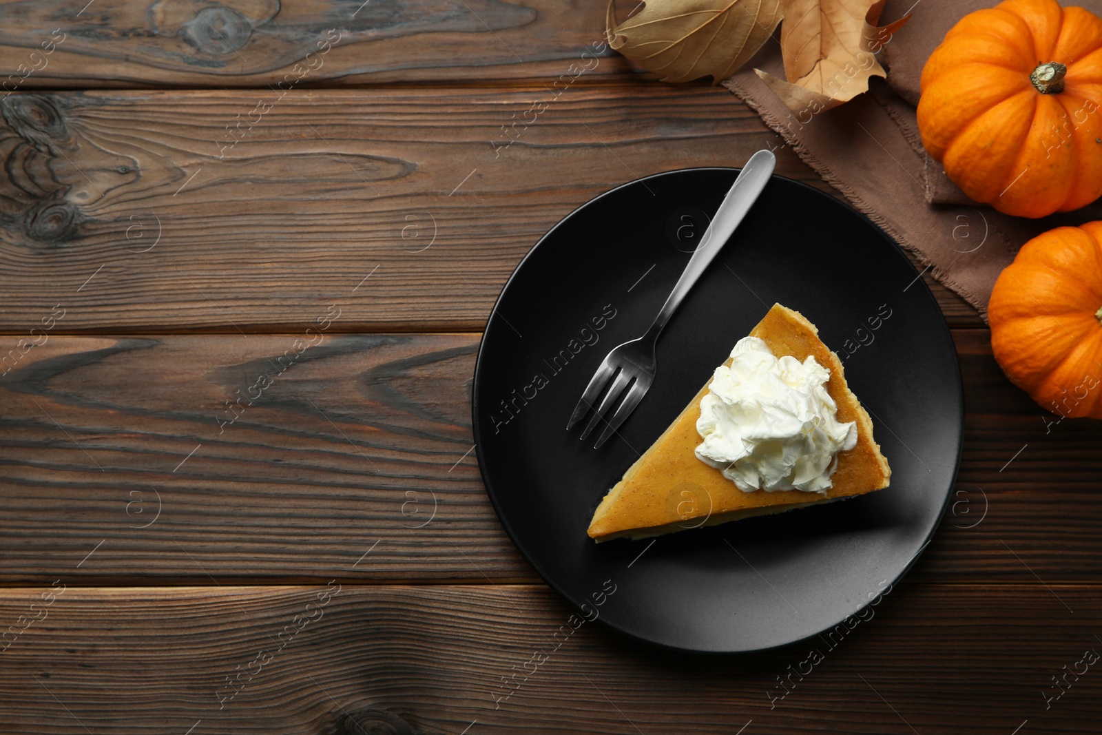 Photo of Piece of delicious pie with whipped cream, pumpkins and fork on wooden table, flat lay. Space for text