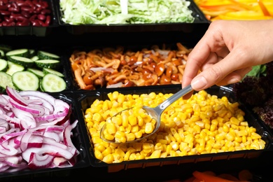 Photo of Young woman taking sweet corn from salad bar, closeup