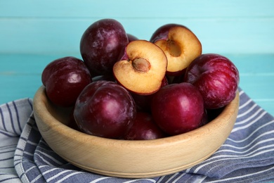 Delicious ripe plums in bowl on light blue background