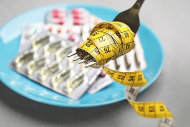 Photo of Fork with measuring tape and blurred pills on background, closeup. Weight loss