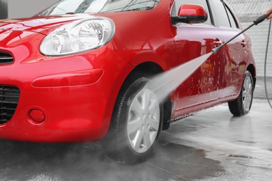 Male worker cleaning vehicle with high pressure water jet at car wash