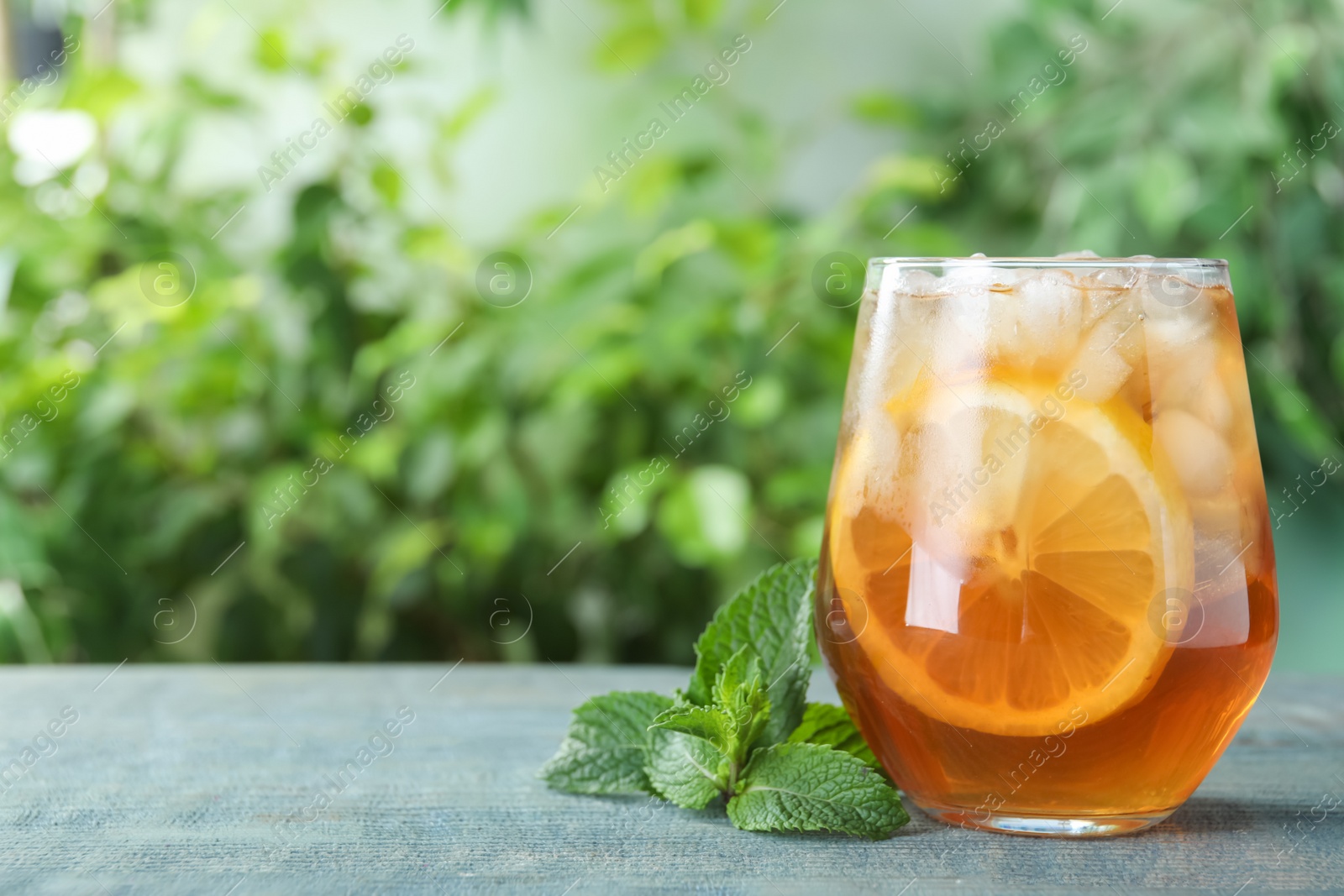 Photo of Delicious iced tea in glass on blue wooden table outdoors, space for text