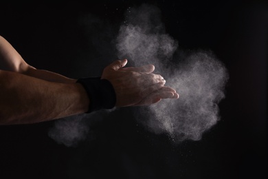 Photo of Young man applying chalk powder on hands against dark background
