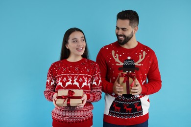 Photo of Happy young couple in Christmas sweaters with gifts on light blue background