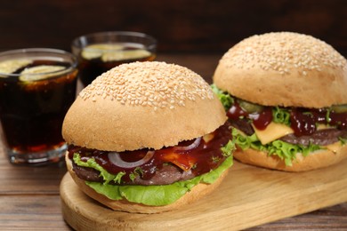 Photo of Board with delicious cheeseburgers on wooden table, closeup