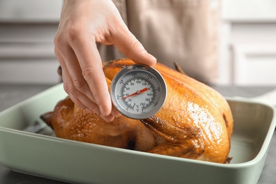 Photo of Woman measuring temperature of whole roasted turkey with meat thermometer, closeup