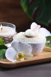 Photo of Natural sea salt in bowl, candle and beautiful orchid flower on wooden table