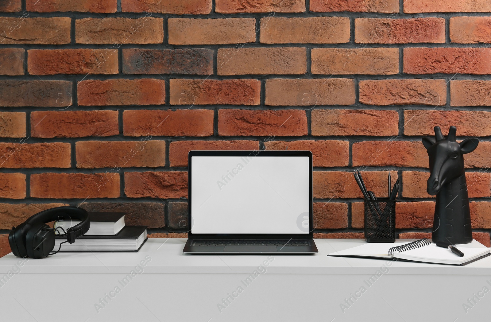 Photo of Stylish workplace with laptop, headphones, stationary and decor on white table near brick wall