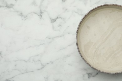 Photo of Beige bowl with water on white marble table, top view. Space for text