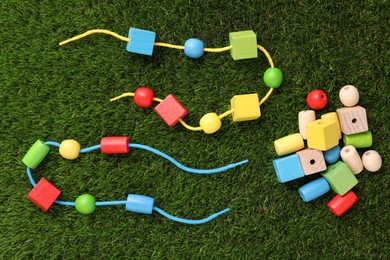 Wooden pieces and strings for threading activity on artificial grass, flat lay. Educational toy for motor skills development