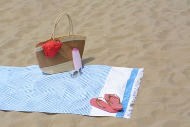 Photo of Light blue striped towel with bag, flip flops, sunglasses and sunblock on sandy beach