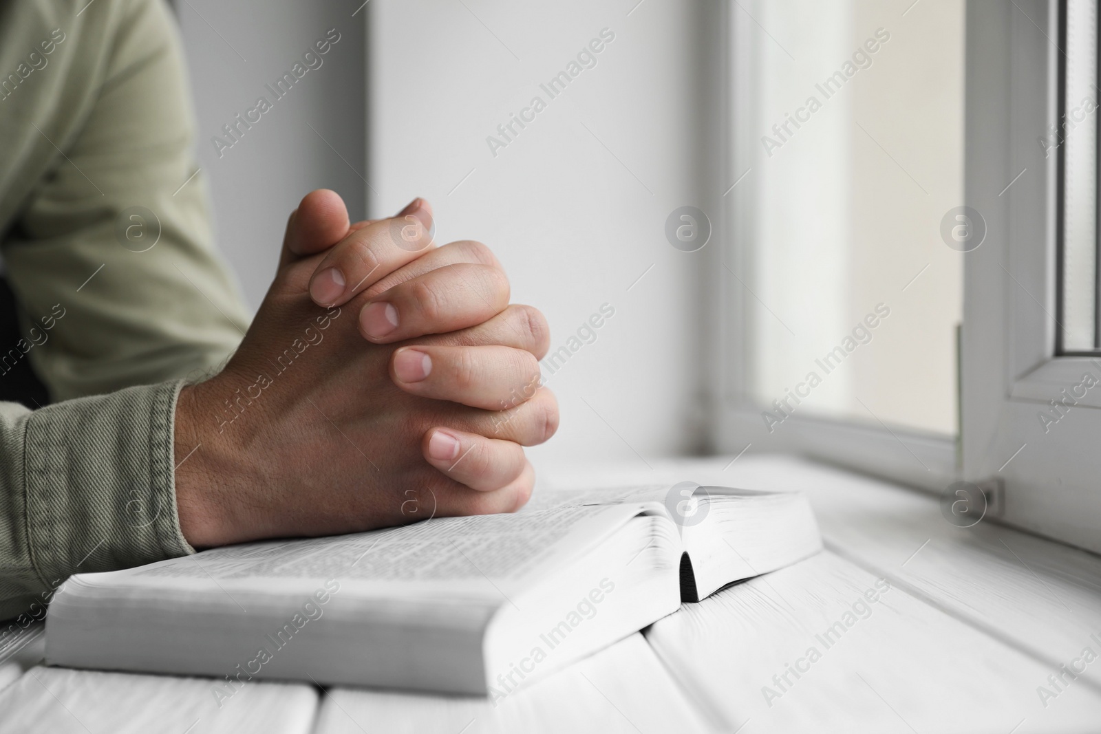 Photo of Religion. Christian man praying over Bible at white wooden the table, closeup