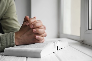 Photo of Religion. Christian man praying over Bible at white wooden the table, closeup