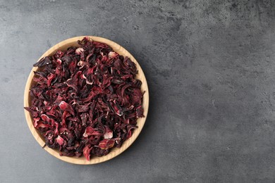 Photo of Hibiscus tea. Wooden bowl with dried roselle calyces on grey table, top view. Space for text
