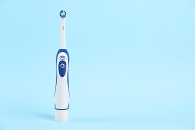 Electric toothbrush on light blue background, space for text