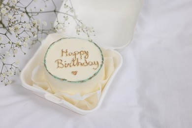 Delicious decorated Birthday cake near dry flowers on white cloth, space for text