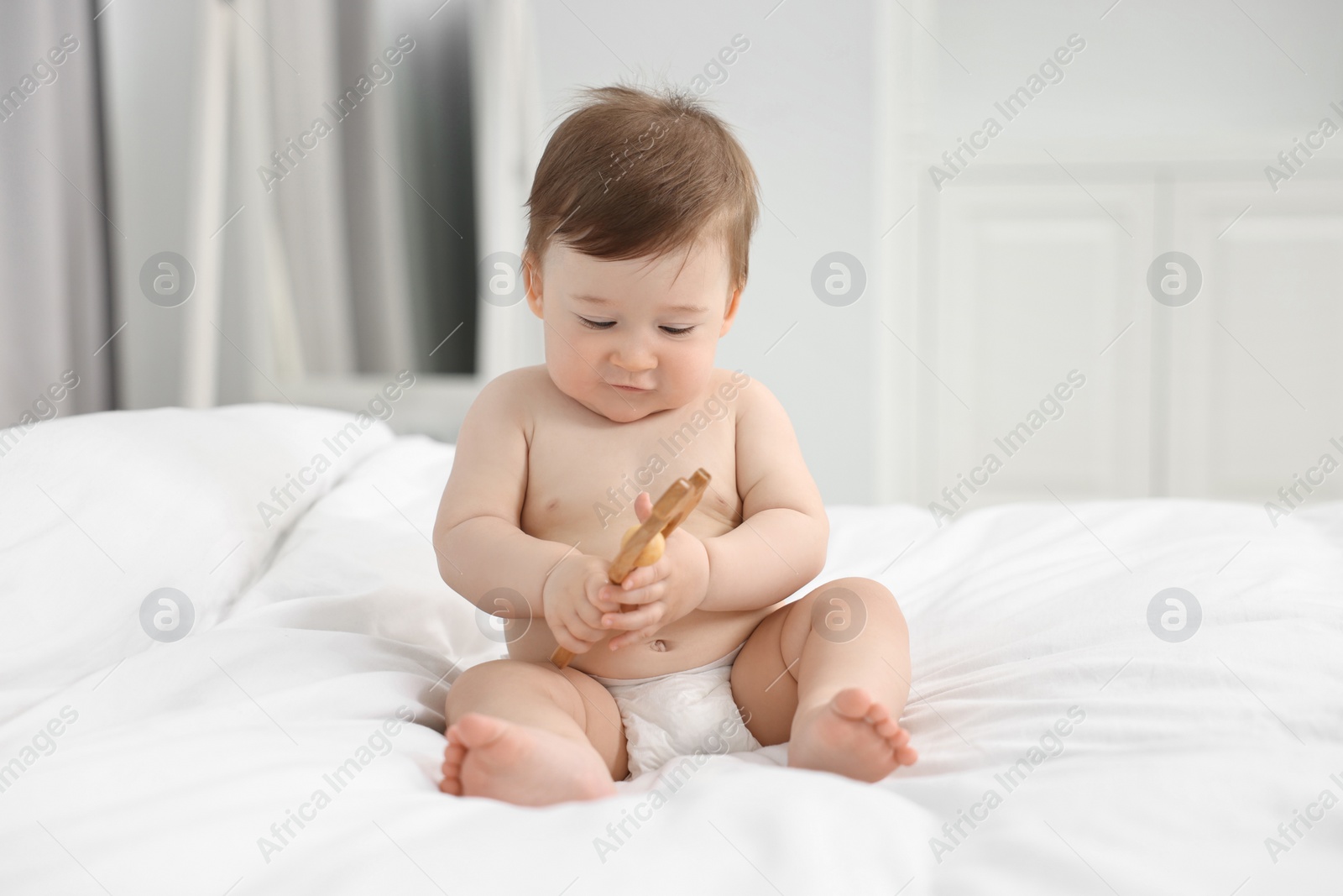 Photo of Cute baby boy with wooden rattle on bed at home