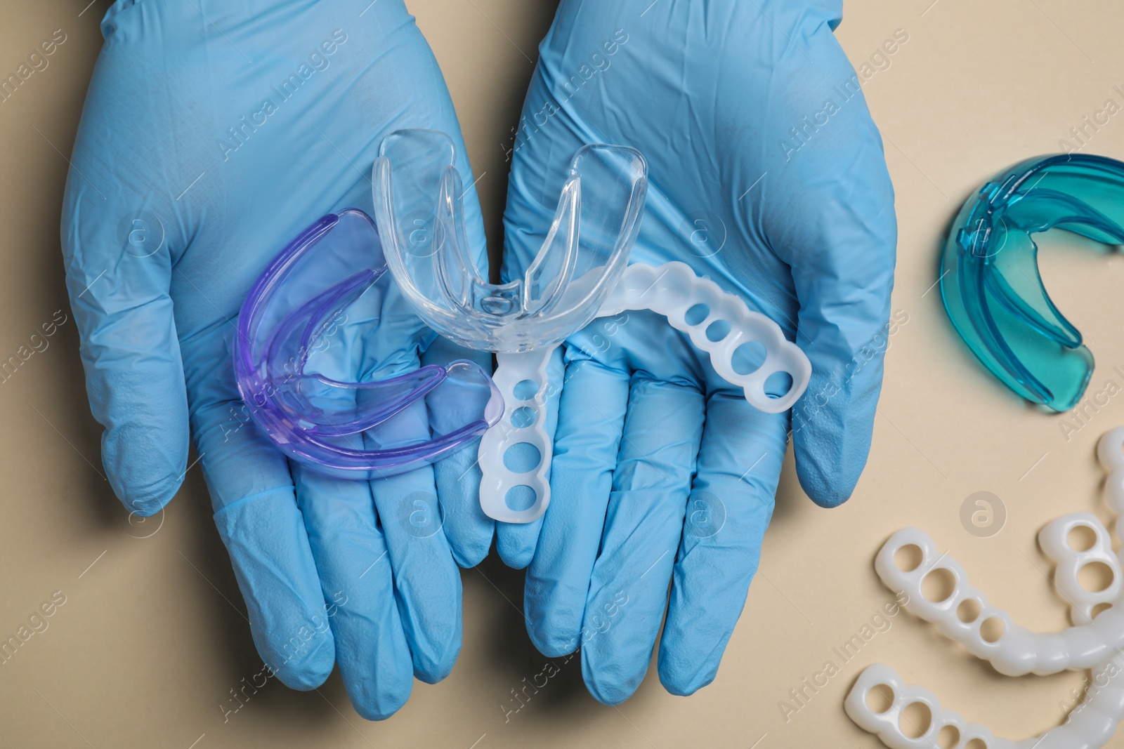 Photo of Bite correction. Dentist in medical gloves holding different mouth guards on beige background, top view