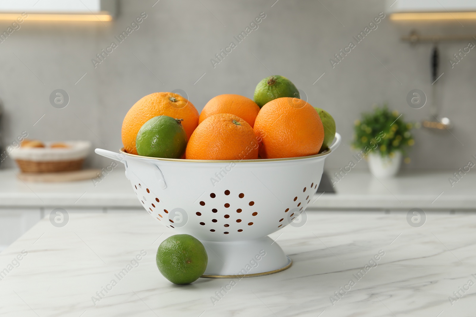 Photo of Colander with fresh fruits on white marble table in kitchen