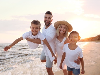 Photo of Happy family having fun on sandy beach near sea at sunset
