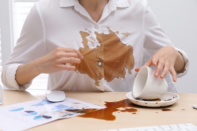 Photo of Woman in dirty shirt at wooden desk with coffee spill, closeup