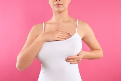 Woman checking her breast on color background, closeup