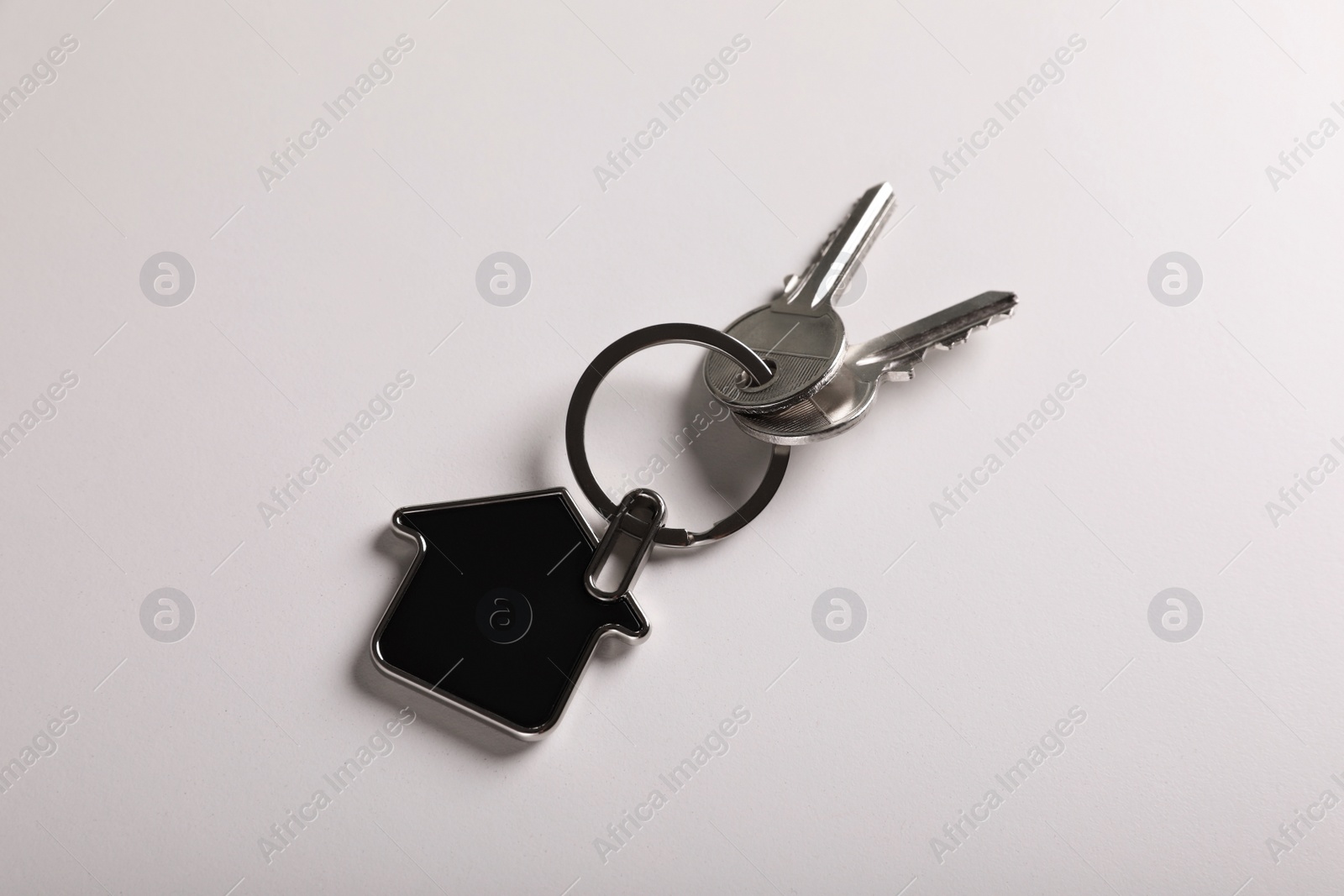 Photo of Keys with trinket in shape of house on white background, top view. Real estate agent services