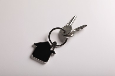 Keys with trinket in shape of house on white background, top view. Real estate agent services