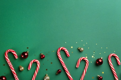 Photo of Candy canes and Christmas balls on green background, flat lay. Space for text