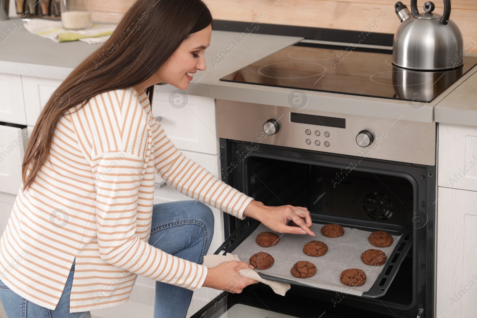 Photo of Beautiful woman taking out tray of baked cookies from oven in kitchen