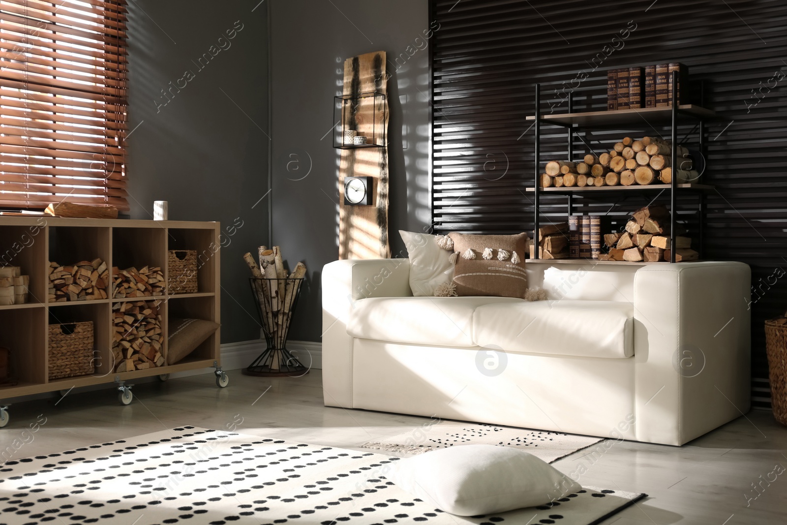 Photo of Shelving unit with stacked firewood and comfortable sofa in stylish room interior