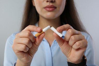 Photo of Stop smoking concept. Woman breaking cigarette on light grey background, closeup