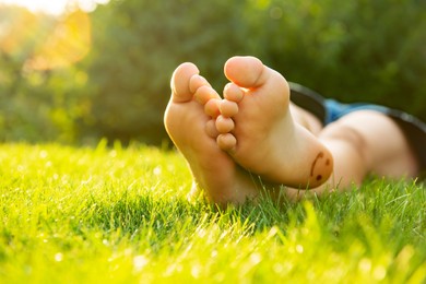 Photo of Teenage girl lying barefoot on green grass outdoors, closeup. Space for text