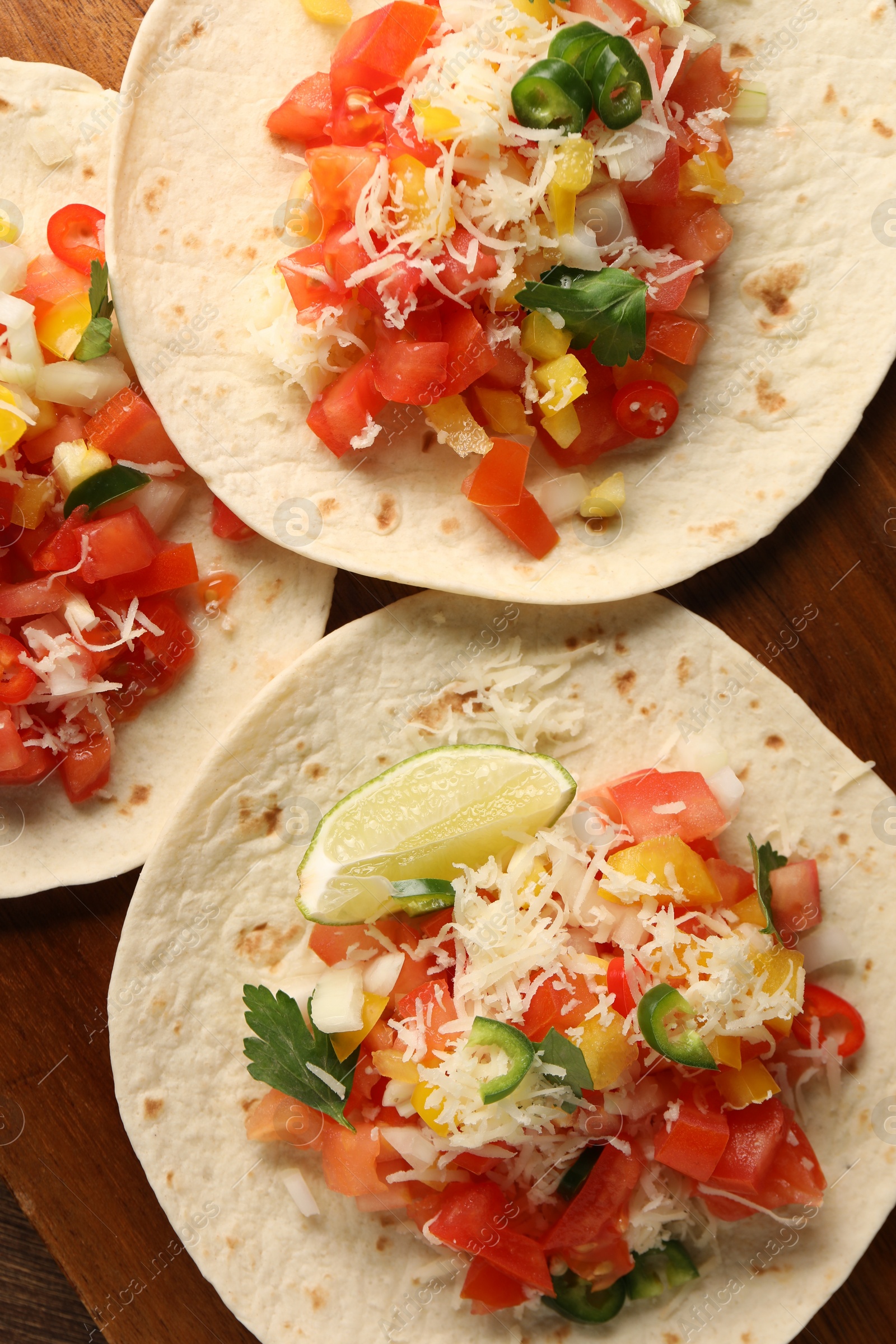 Photo of Delicious tacos with vegetables and lime on wooden table, top view