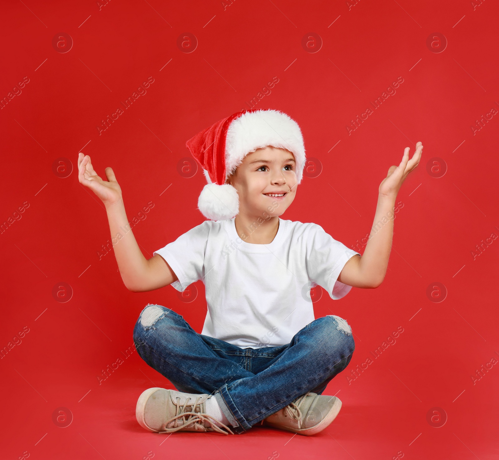 Photo of Cute little child wearing Santa hat on red background. Christmas holiday