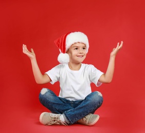 Cute little child wearing Santa hat on red background. Christmas holiday