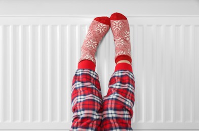 Little girl warming feet near heating radiator indoors, closeup