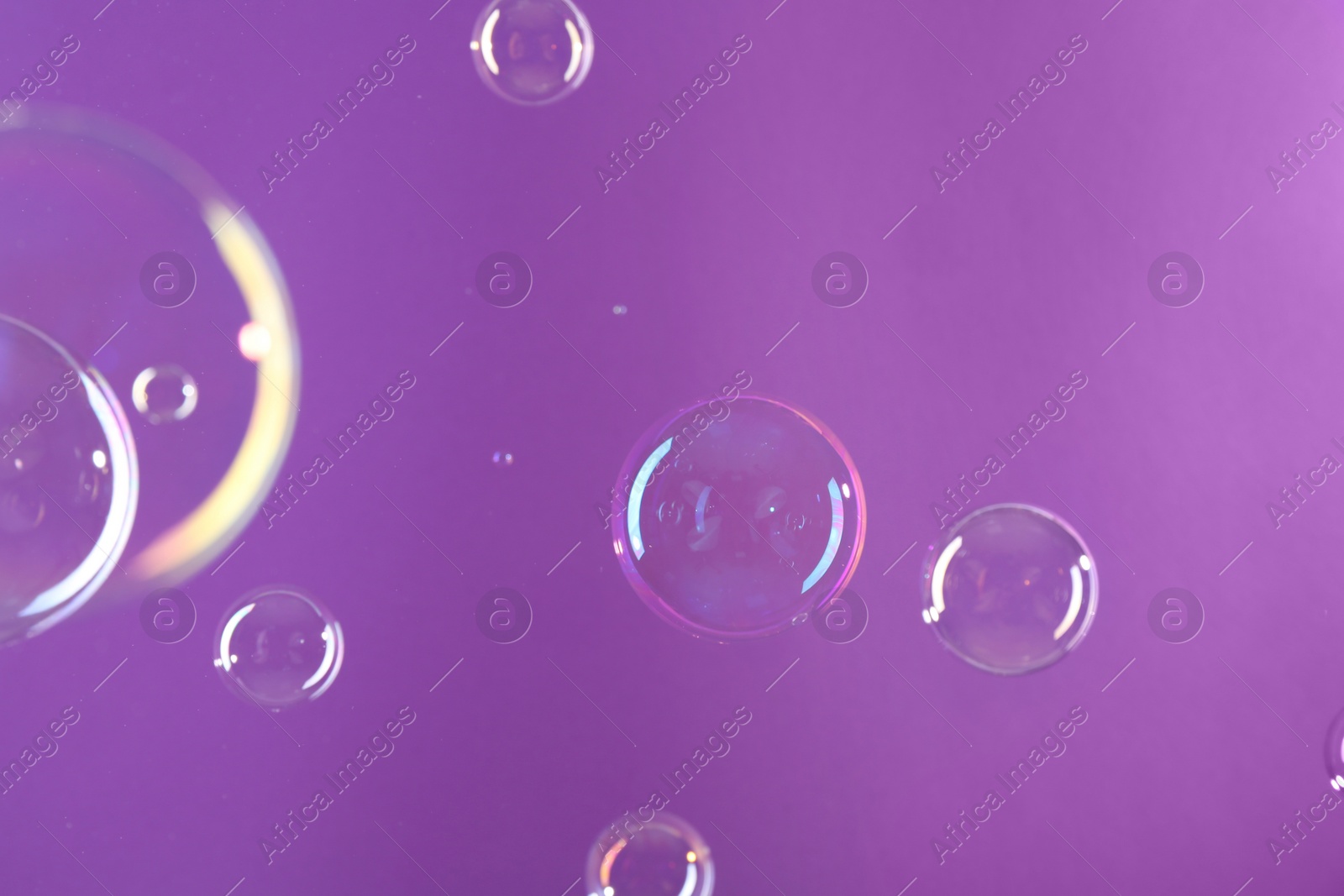 Photo of Beautiful transparent soap bubbles on violet background