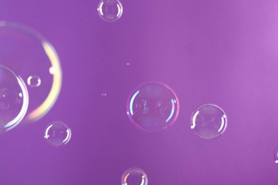 Beautiful transparent soap bubbles on violet background