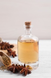 Photo of Bottle of essential oil, anise and seeds on white wooden table