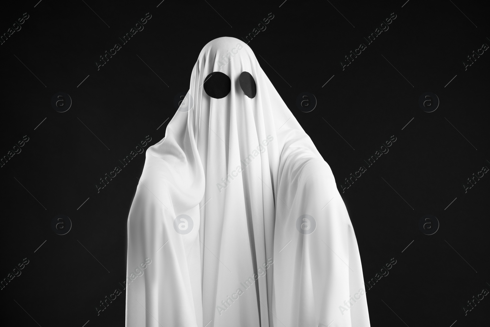 Photo of Creepy ghost. Person covered with white sheet on black background