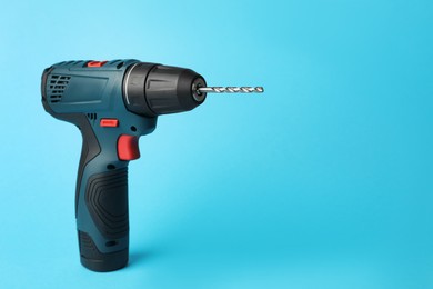 Photo of Modern electric power drill on light blue background, space for text