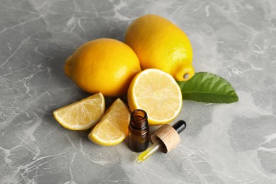 Photo of Bottle of essential oil with lemons on grey marble table