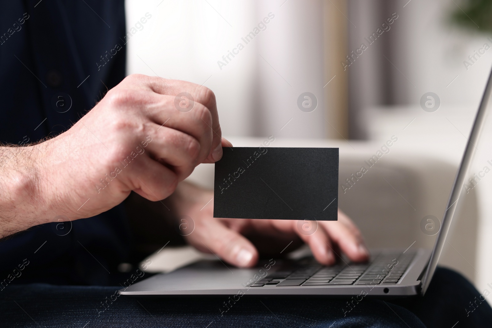 Photo of Man with laptop holding blank business card on blurred background, closeup