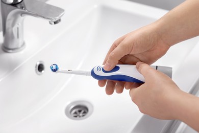 Woman holding electric toothbrush above sink in bathroom, closeup